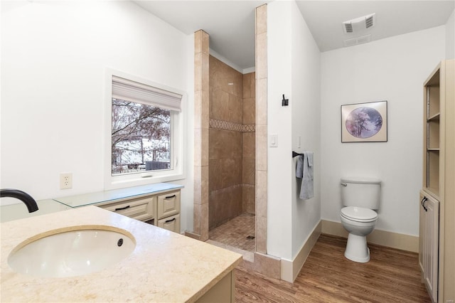 bathroom with vanity, toilet, wood-type flooring, and tiled shower