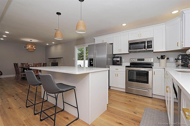 kitchen with hanging light fixtures, stainless steel appliances, a kitchen island, light hardwood / wood-style flooring, and white cabinets