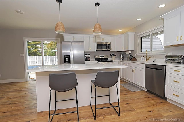 kitchen featuring a kitchen island, white cabinetry, hanging light fixtures, and appliances with stainless steel finishes