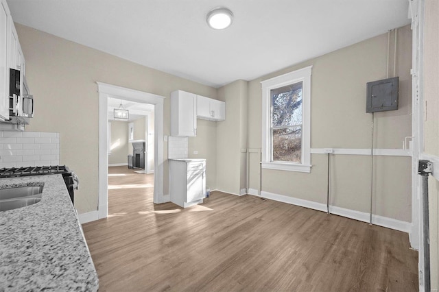 kitchen featuring light stone countertops, light hardwood / wood-style flooring, backsplash, electric panel, and white cabinets