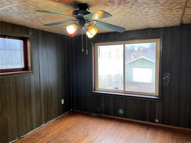 spare room featuring a wealth of natural light, hardwood / wood-style flooring, ceiling fan, and wood walls