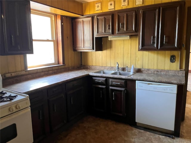 kitchen featuring dark brown cabinetry, wooden walls, sink, and white appliances