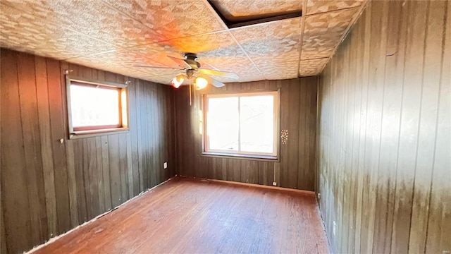 empty room with ceiling fan, plenty of natural light, wooden walls, and hardwood / wood-style flooring