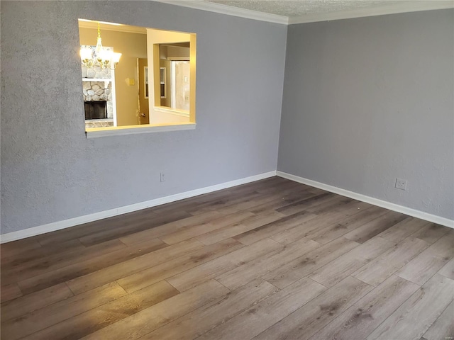 empty room with hardwood / wood-style floors, a stone fireplace, crown molding, a textured ceiling, and a notable chandelier