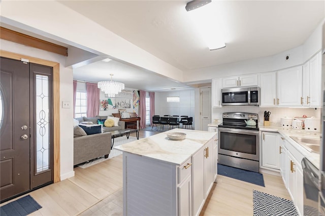 kitchen with a notable chandelier, a center island, white cabinets, decorative light fixtures, and stainless steel appliances