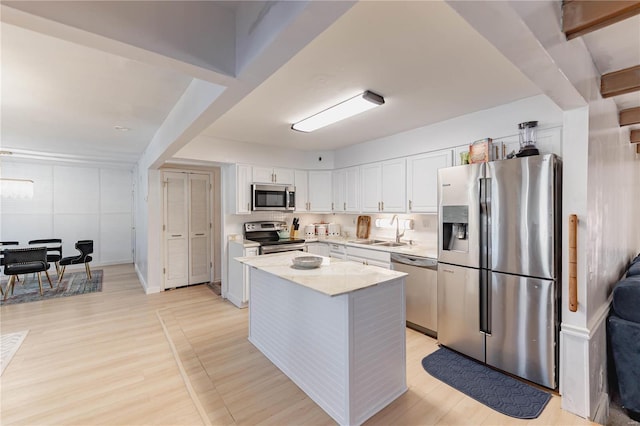 kitchen featuring a center island, white cabinetry, stainless steel appliances, sink, and light stone counters