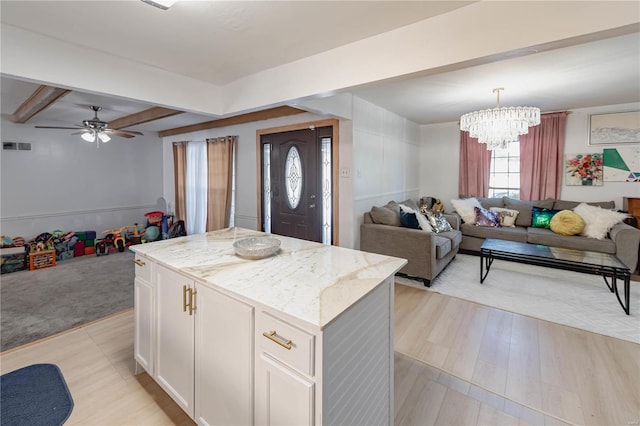 kitchen with light stone countertops, a kitchen island, decorative light fixtures, white cabinetry, and beam ceiling