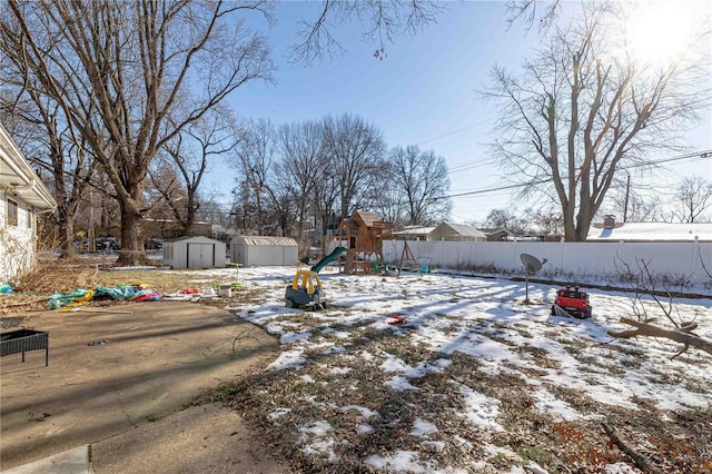 snowy yard featuring a playground and a storage unit