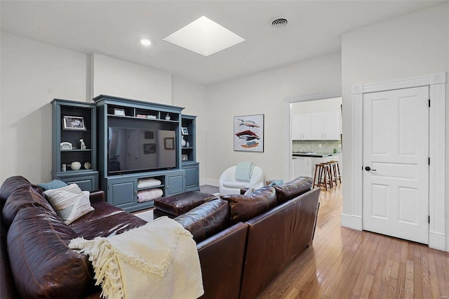 living room featuring a skylight and light hardwood / wood-style flooring