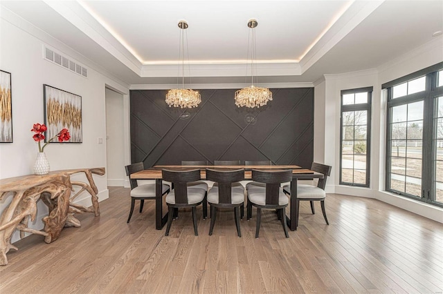 dining area featuring hardwood / wood-style flooring, a notable chandelier, a raised ceiling, and ornamental molding