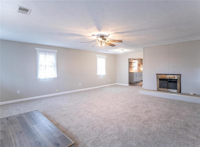 unfurnished living room featuring baseboards, visible vents, a ceiling fan, light colored carpet, and a glass covered fireplace