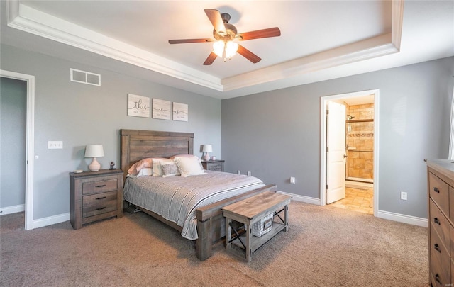 bedroom featuring ceiling fan, ensuite bathroom, light carpet, and a tray ceiling