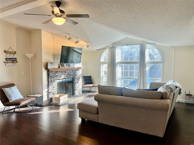 living room with rail lighting, ceiling fan, dark hardwood / wood-style floors, a stone fireplace, and lofted ceiling