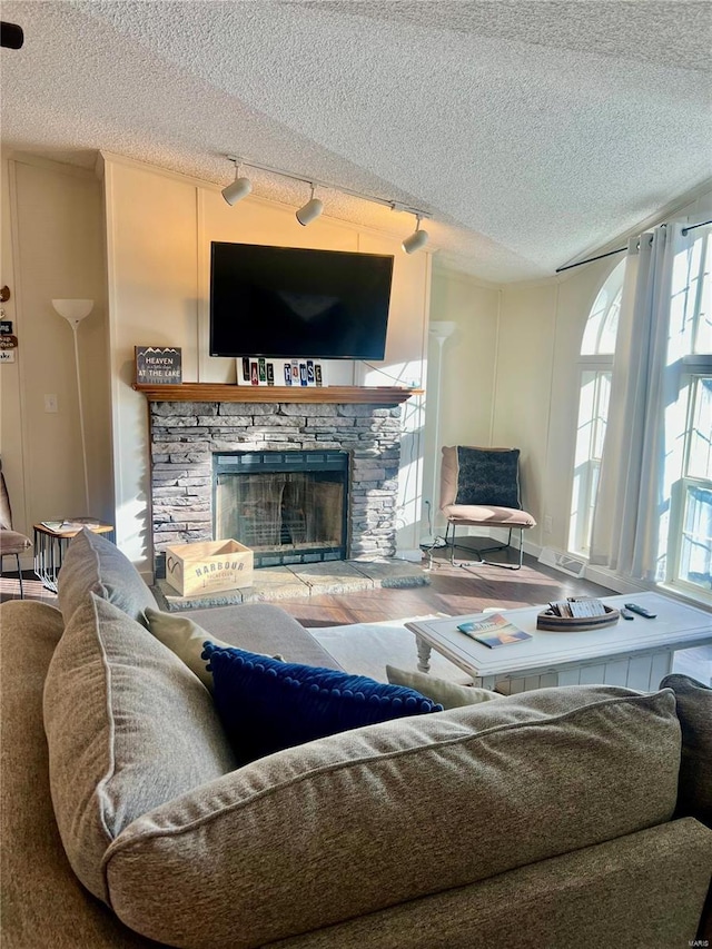 living room with a textured ceiling, rail lighting, a stone fireplace, and hardwood / wood-style floors