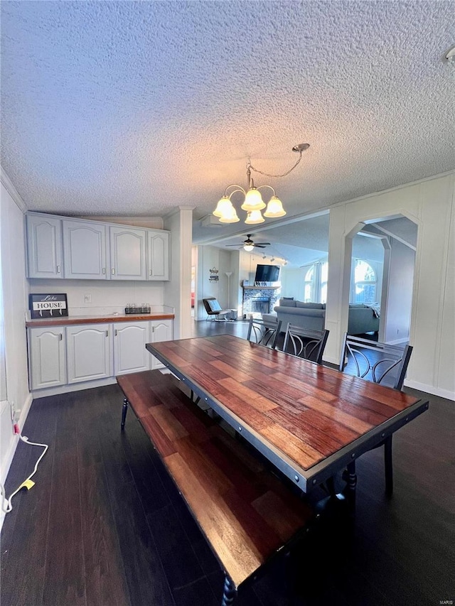 dining room with a textured ceiling, ceiling fan with notable chandelier, and dark wood-type flooring