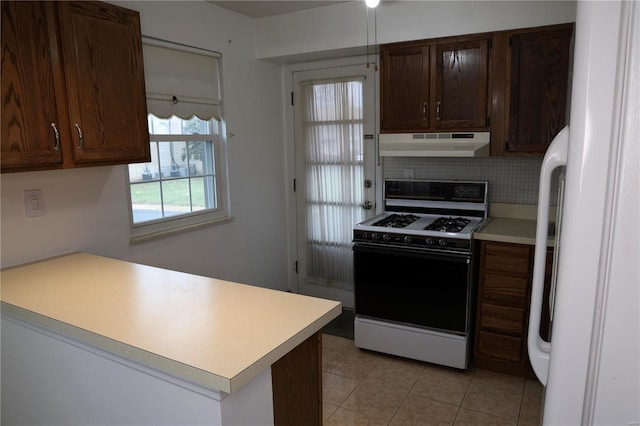 kitchen with tasteful backsplash, white gas range, kitchen peninsula, and light tile patterned floors