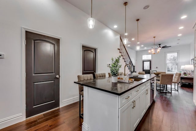 kitchen with a kitchen island with sink, ceiling fan, dark hardwood / wood-style floors, white cabinetry, and a breakfast bar area