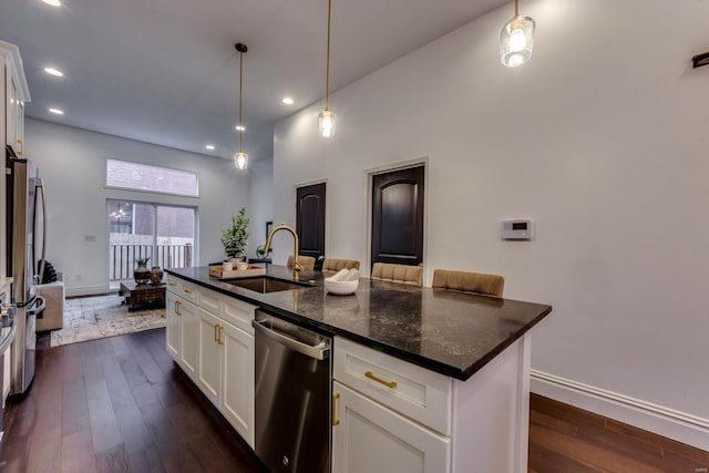 kitchen with dark stone counters, stainless steel appliances, a kitchen island with sink, sink, and white cabinetry