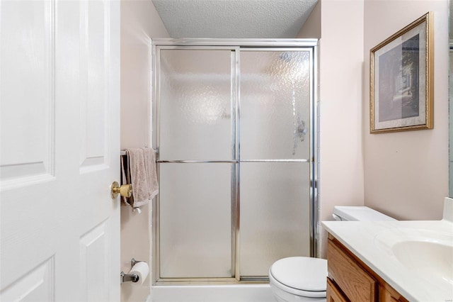 bathroom featuring a textured ceiling, toilet, a shower with shower door, and vanity