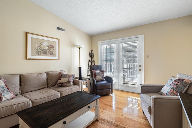 living room with vaulted ceiling, a textured ceiling, and light hardwood / wood-style flooring