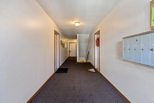 hallway featuring a mail area, a textured ceiling, and dark colored carpet