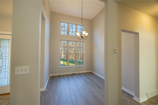 unfurnished dining area featuring a notable chandelier, dark hardwood / wood-style flooring, a towering ceiling, and plenty of natural light