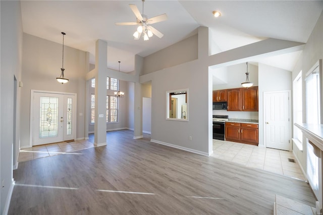 unfurnished living room with ceiling fan with notable chandelier, light hardwood / wood-style floors, and high vaulted ceiling