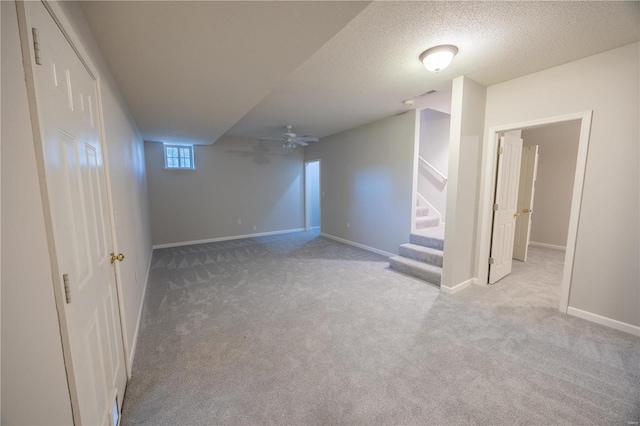 basement with ceiling fan, light colored carpet, and a textured ceiling