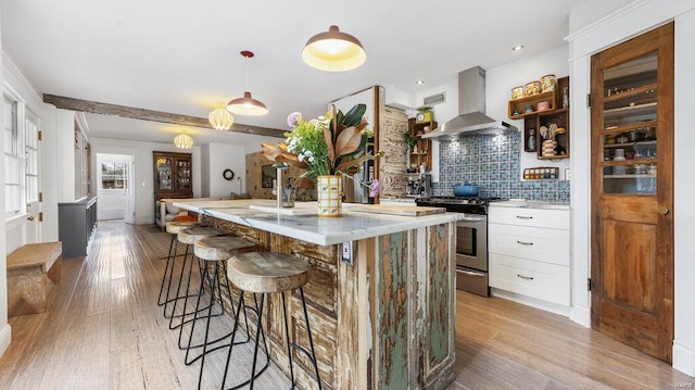 kitchen featuring pendant lighting, backsplash, white cabinets, stainless steel stove, and range hood