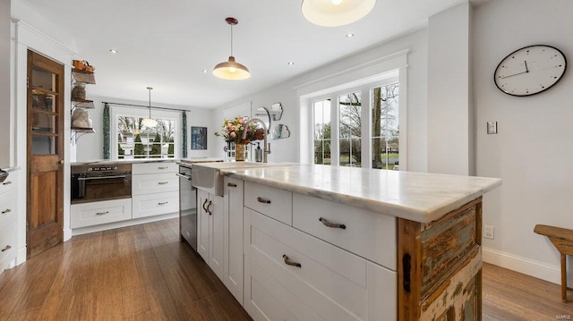 kitchen featuring a wealth of natural light, white cabinetry, a center island, oven, and hanging light fixtures