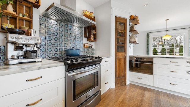 kitchen featuring white cabinetry, hanging light fixtures, wall chimney range hood, tasteful backsplash, and stainless steel range with gas stovetop