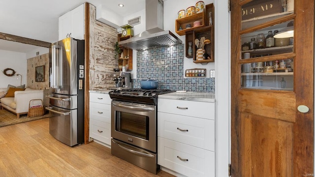 kitchen featuring backsplash, exhaust hood, white cabinets, light wood-type flooring, and stainless steel appliances