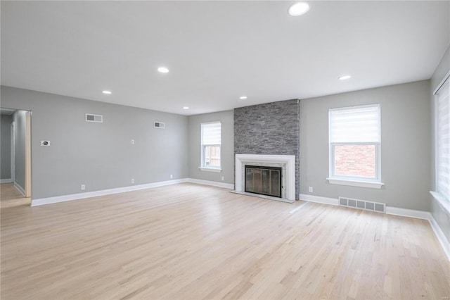 unfurnished living room featuring light wood-type flooring and a stone fireplace