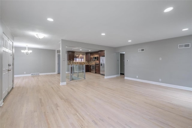 unfurnished living room featuring a notable chandelier and light wood-type flooring