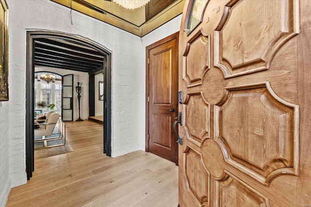 interior space with brick wall, a chandelier, and light wood-type flooring