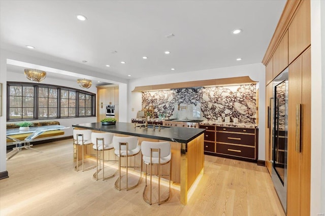 kitchen with a breakfast bar, tasteful backsplash, sink, a center island with sink, and light wood-type flooring