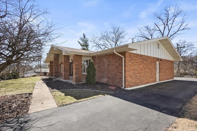 view of side of property featuring a garage, brick siding, board and batten siding, and a lawn