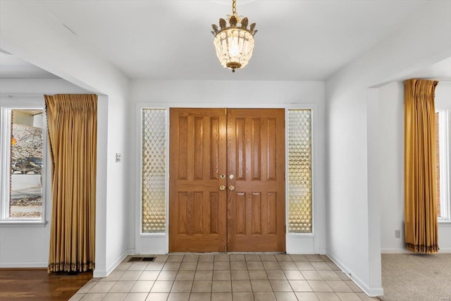 tiled foyer entrance featuring a chandelier, visible vents, and baseboards