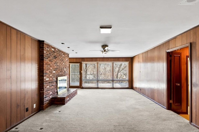 carpeted spare room with a brick fireplace, a ceiling fan, and wood walls