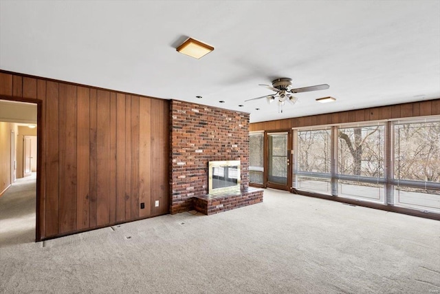 unfurnished living room with wooden walls, carpet, a fireplace, and ceiling fan