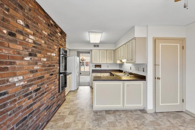 kitchen with a peninsula, a sink, visible vents, freestanding refrigerator, and dark countertops