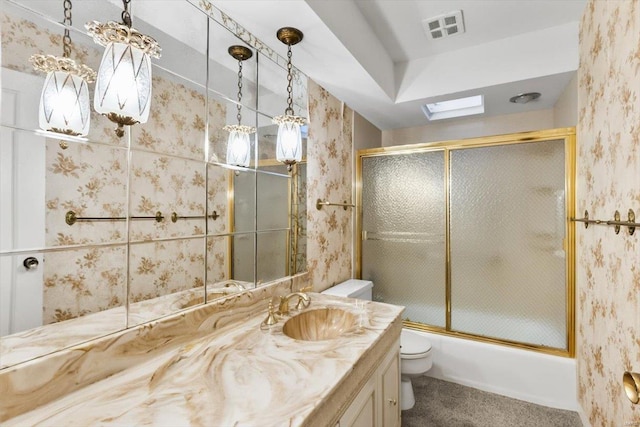 bathroom featuring a skylight, visible vents, toilet, combined bath / shower with glass door, and vanity