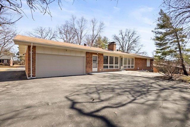 view of front of house featuring driveway, brick siding, a chimney, and an attached garage