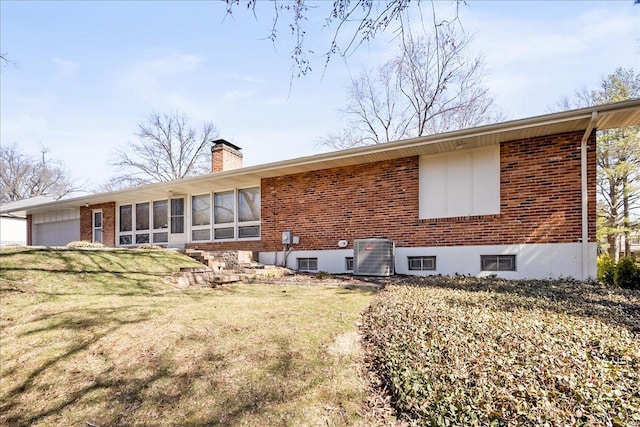 rear view of property with central air condition unit, a chimney, a lawn, and brick siding