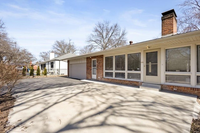 exterior space featuring aphalt driveway, a garage, brick siding, fence, and a chimney