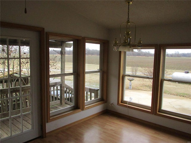 unfurnished dining area featuring vaulted ceiling, light wood-type flooring, a rural view, and a notable chandelier