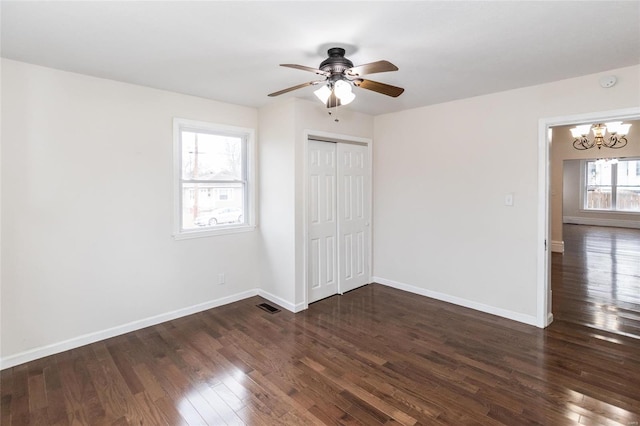 unfurnished bedroom featuring multiple windows, dark hardwood / wood-style flooring, ceiling fan with notable chandelier, and a closet