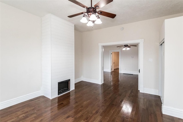 unfurnished living room with a textured ceiling, ceiling fan, a large fireplace, and dark wood-type flooring