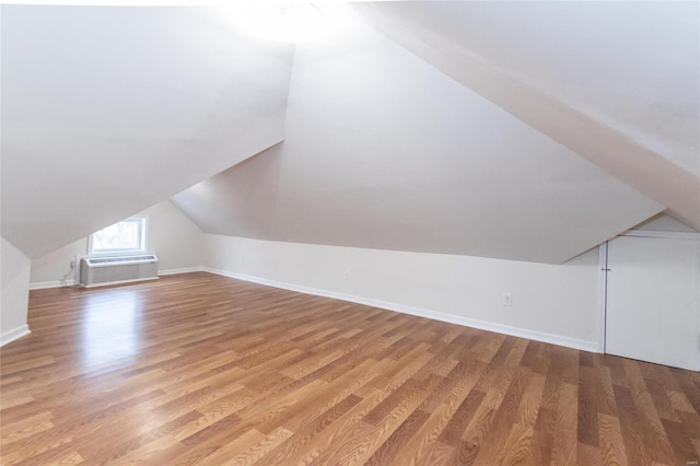 additional living space featuring a wall mounted air conditioner, light hardwood / wood-style floors, and lofted ceiling