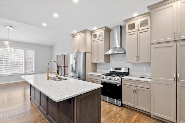 kitchen featuring appliances with stainless steel finishes, wall chimney exhaust hood, a kitchen island with sink, sink, and pendant lighting